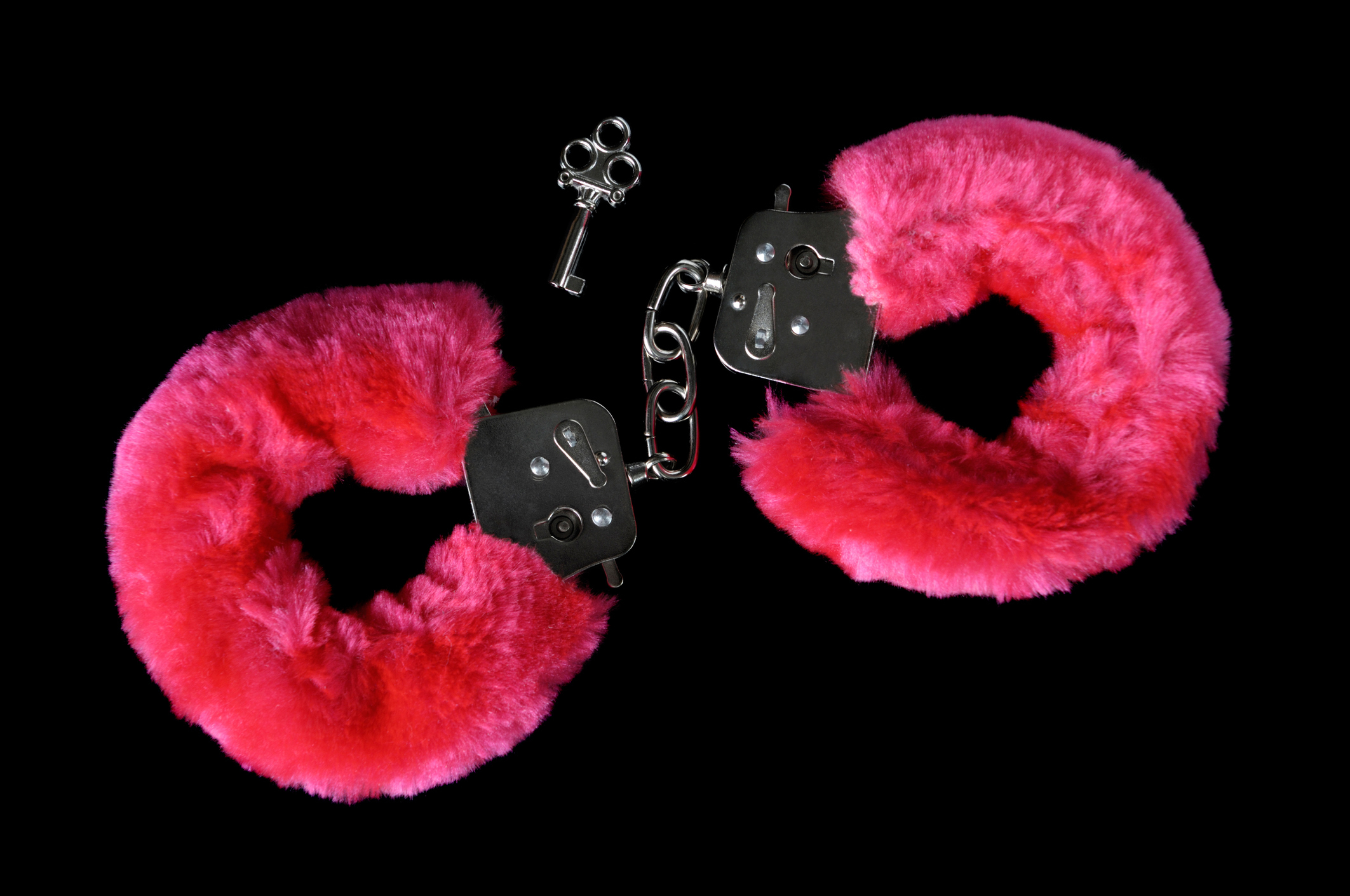 Pink fluffy handcuffs and a small key are placed against a black background