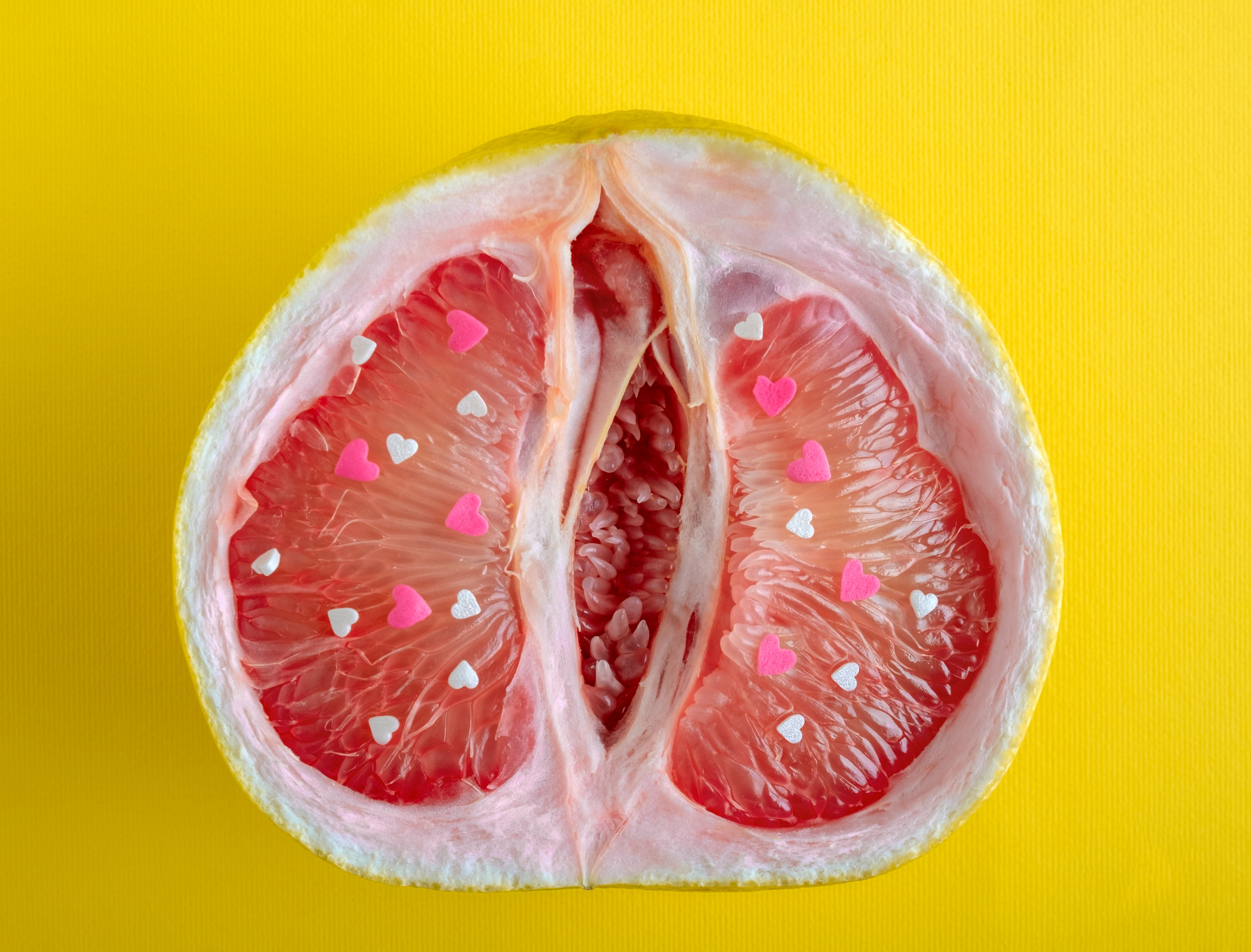 A halved grapefruit with pink and white paper hearts on the segments, set against a yellow background