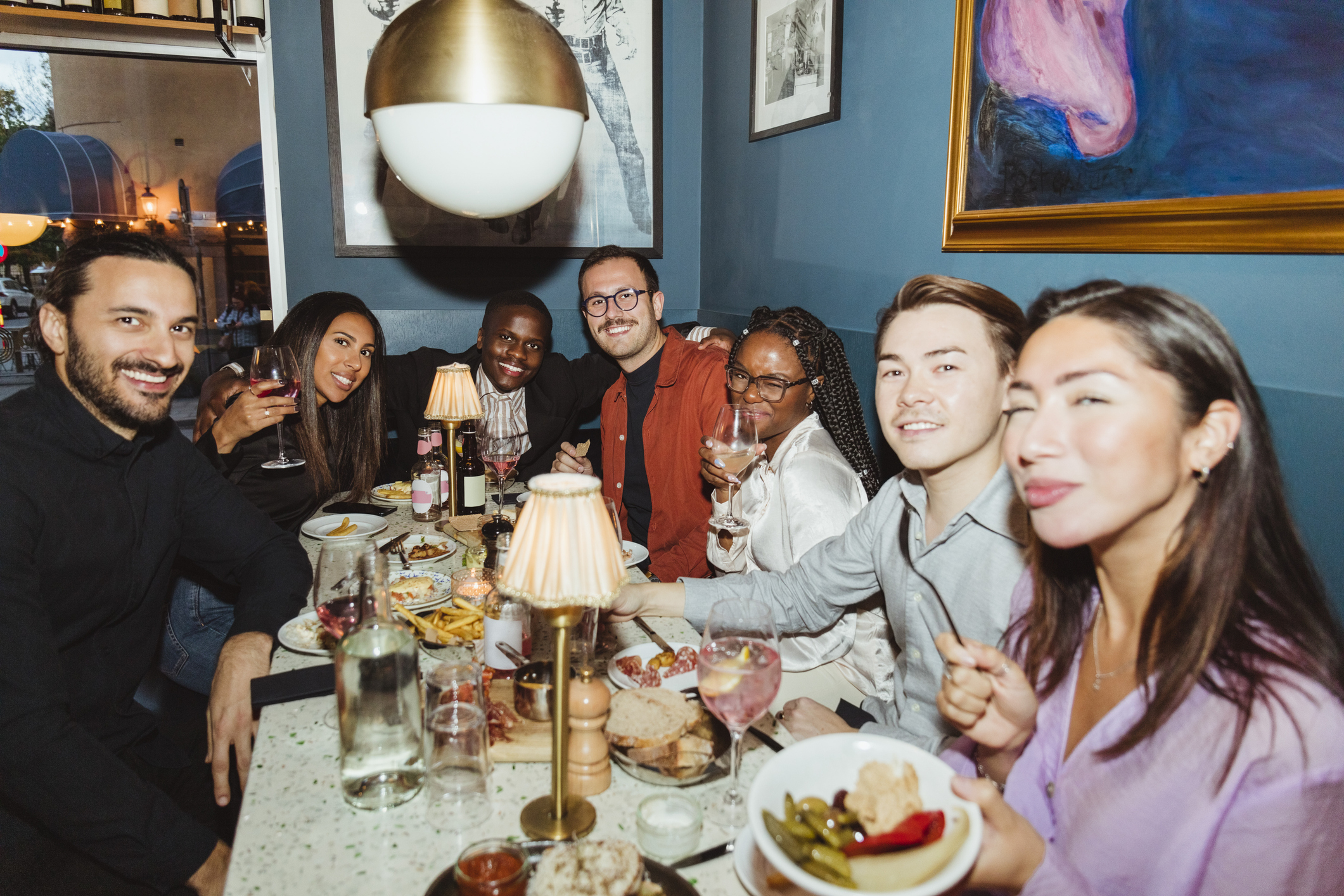 Group of friends enjoying a meal at a restaurant, holding drinks and smiling at the camera