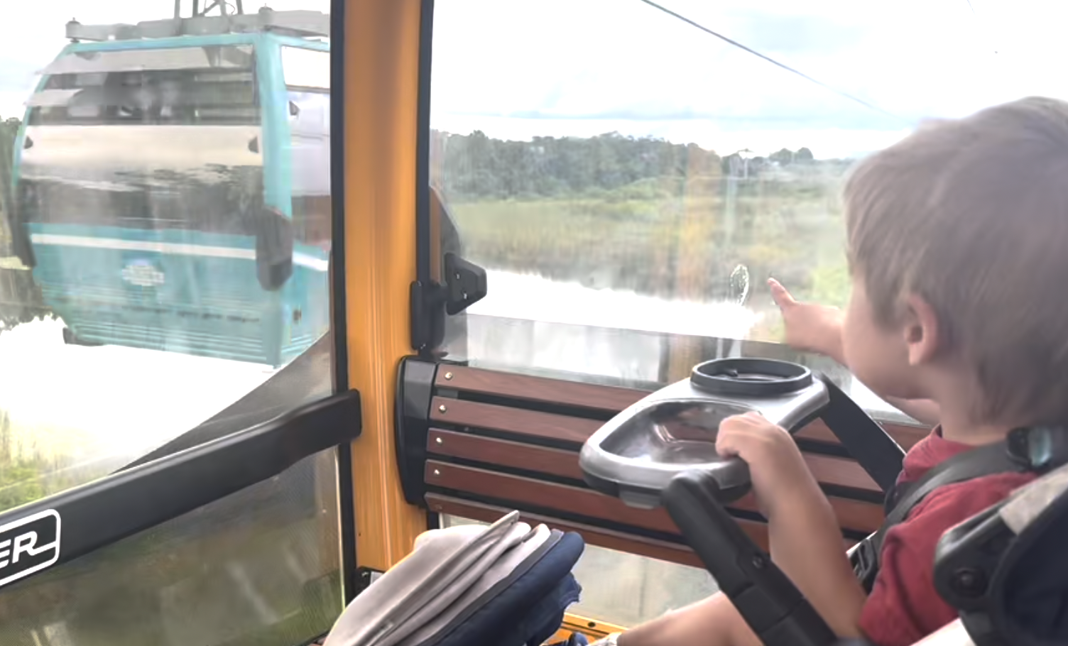 A child points towards another gondola seen through the window during a cable car ride