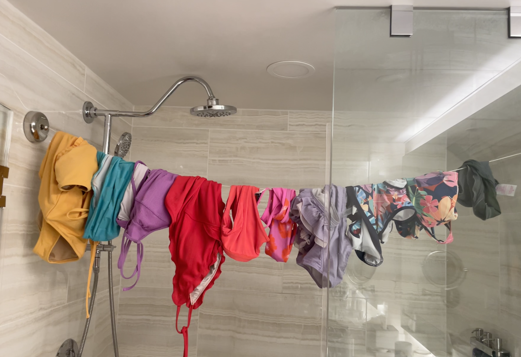 Various swimsuits and clothing items are hung over a shower rod in a bathroom