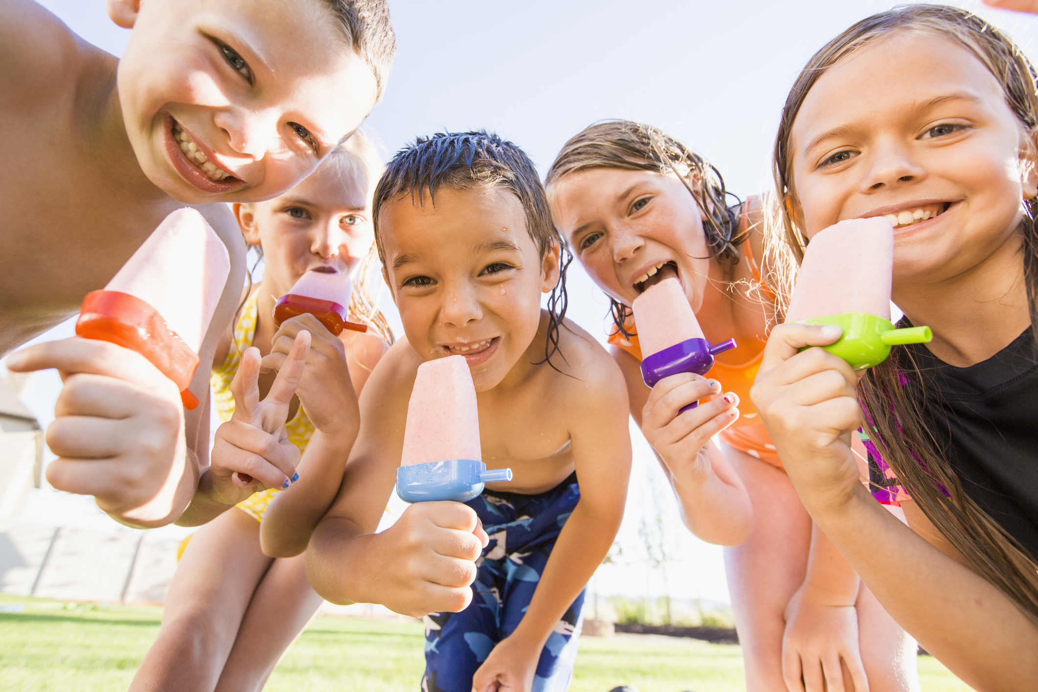 Children enjoying popsicles and smiling at the camera on a sunny day