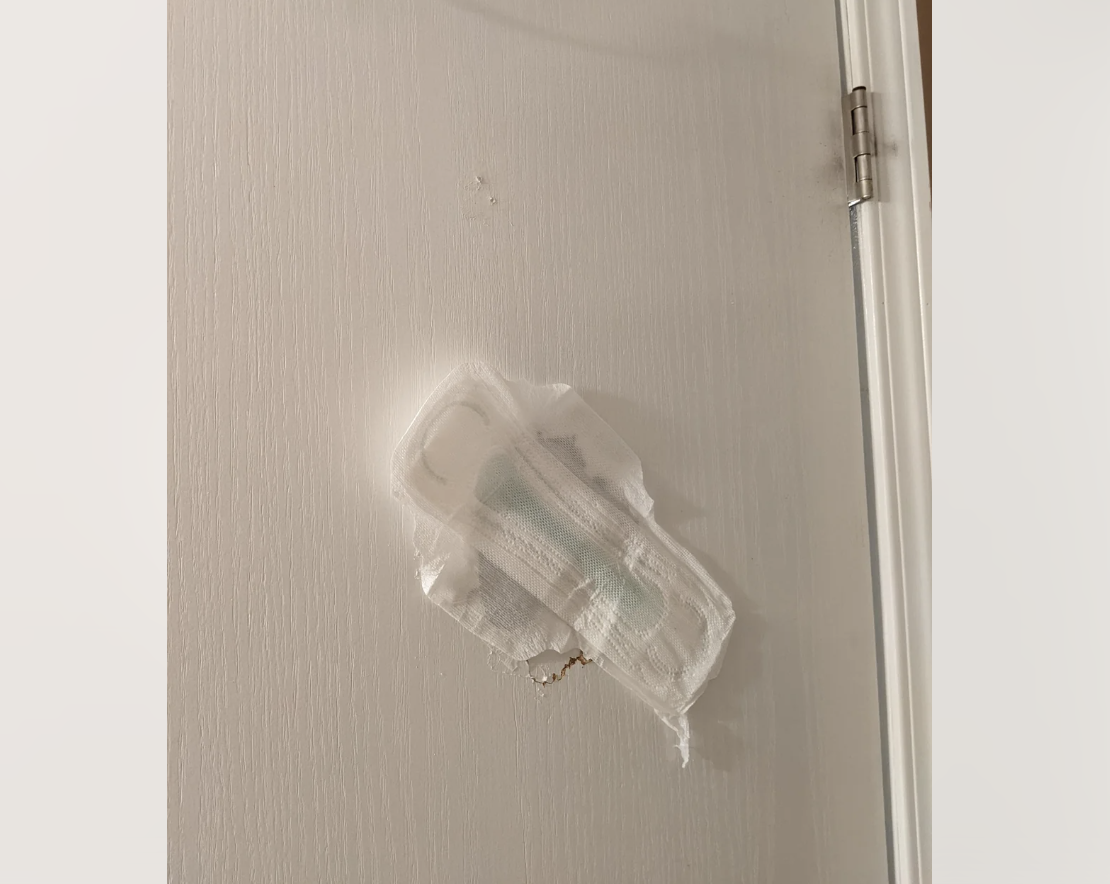 Door with damage repaired by taping a sanitary pad over the hole near the hinges