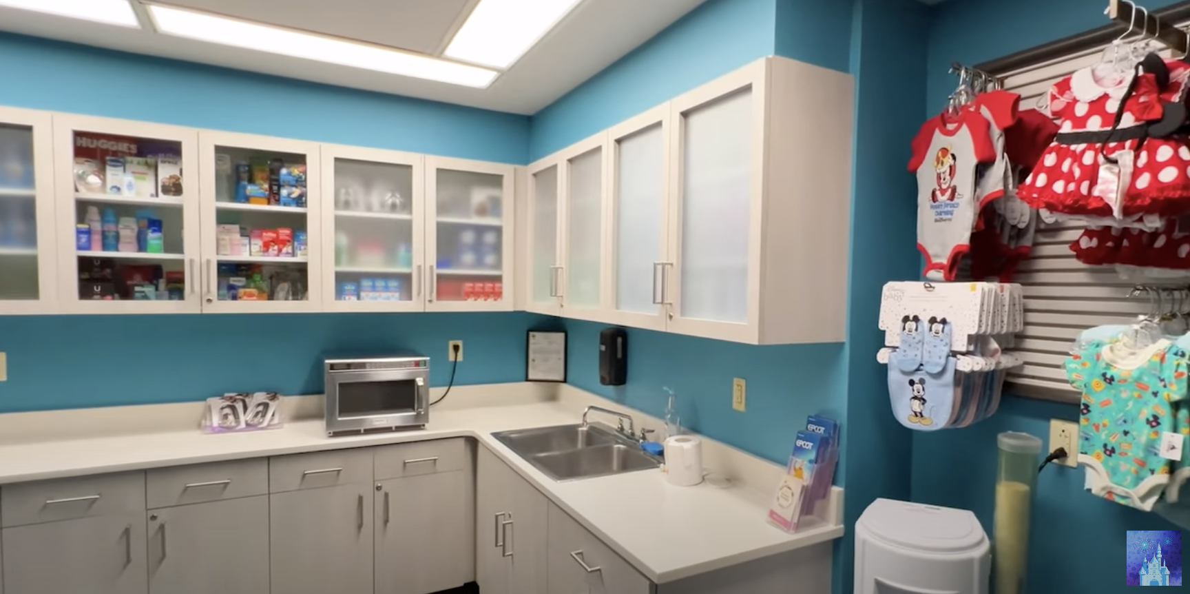 A tidy, well-organized clinic room, with medical supplies in glass cabinets, a microwave, sink, and Disney-themed children&#x27;s clothes hanging on the wall