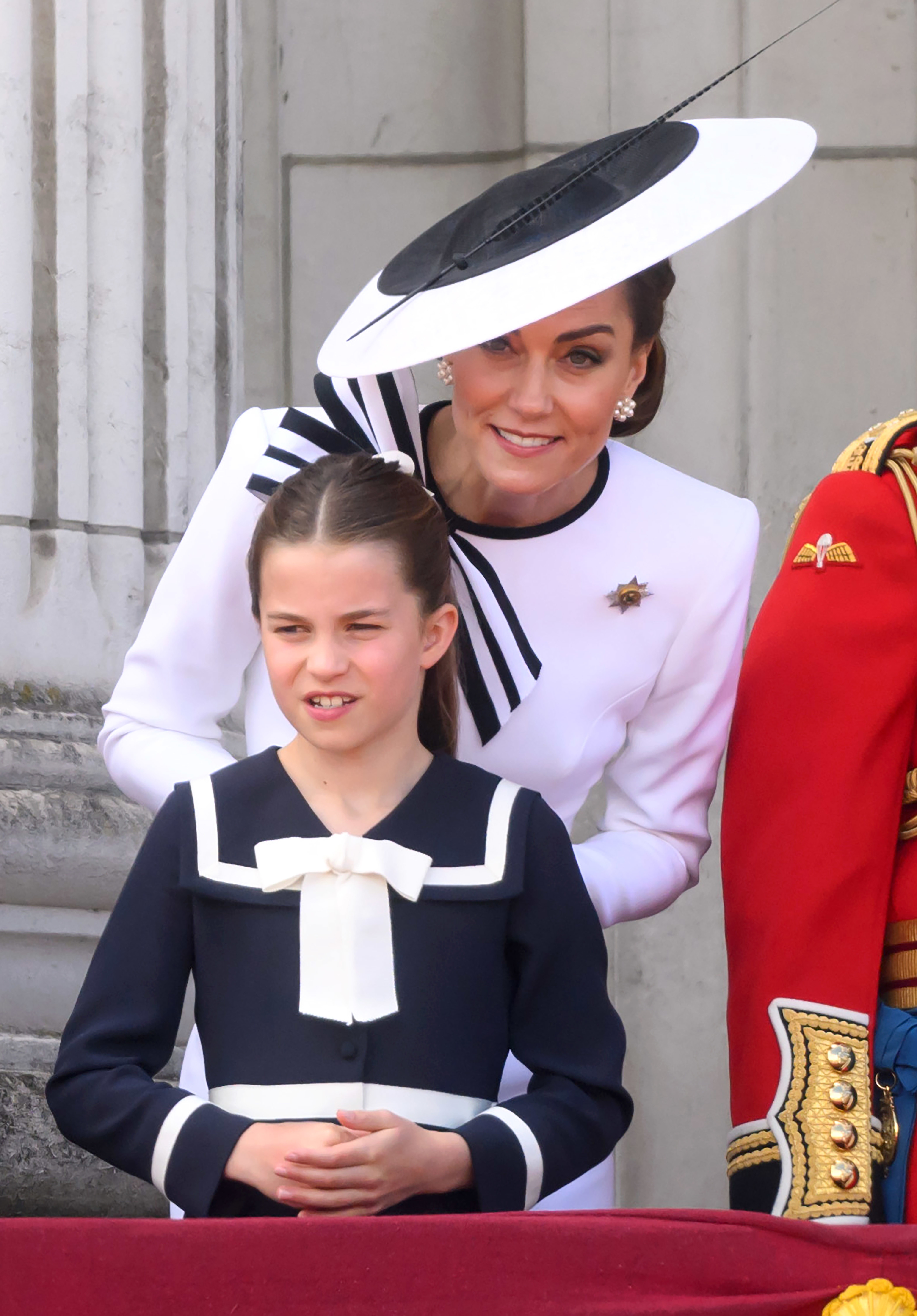 Princess Charlotte, in a navy outfit with a bow, accompanied by Catherine, Duchess of Cambridge, in a dress with a large hat, at an outdoor event