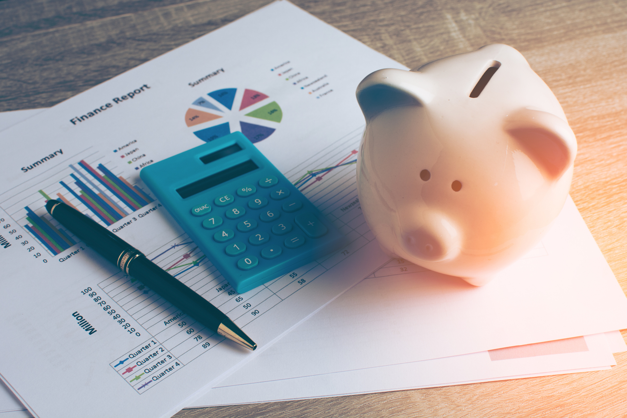 Piggy bank, calculator, and pen on top of financial reports with graphs and charts