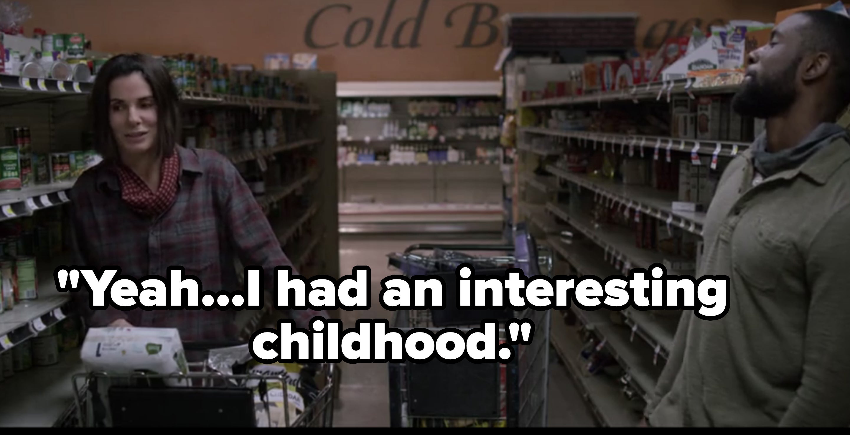 Sandra Bullock and Trevante Rhodes are shopping in a grocery store aisle, pushing carts filled with various items and standing in front of a &quot;Cold Beverages&quot; sign