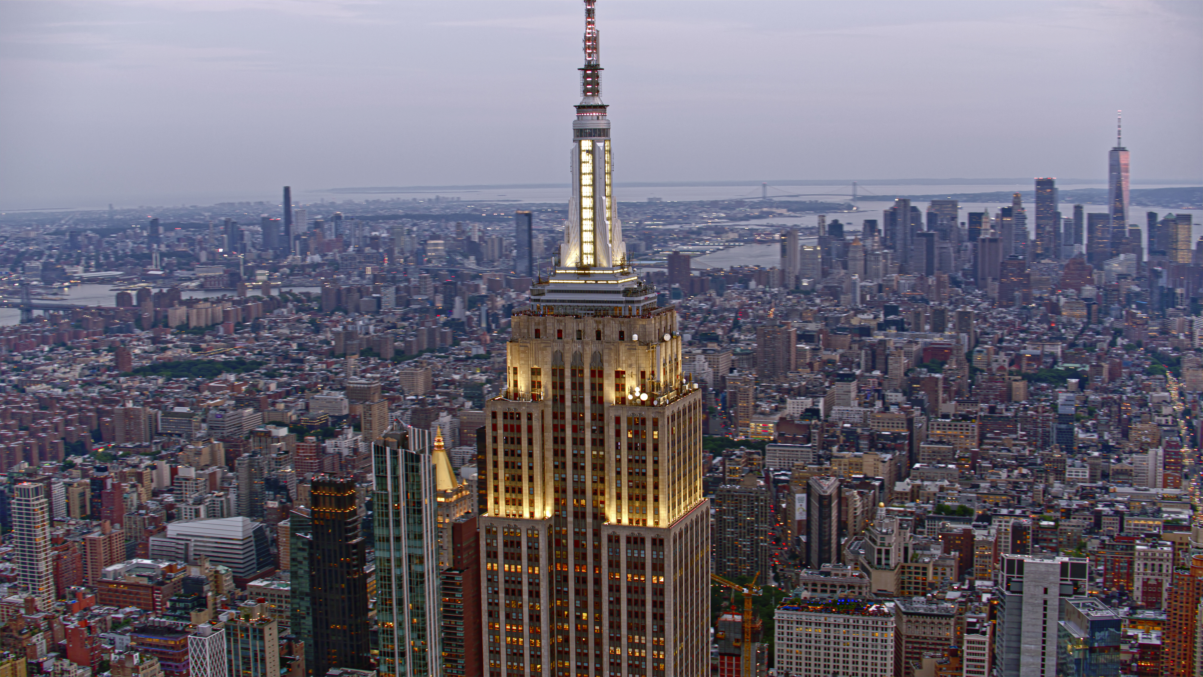 Aerial view of the Empire State Building with a vast cityscape of New York City in the background, showcasing numerous buildings and distant waterways