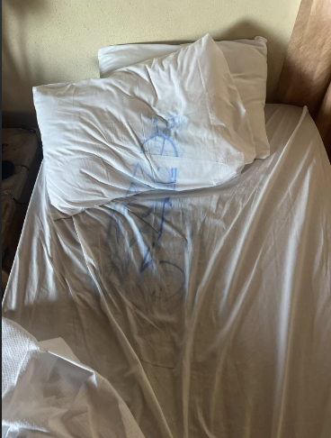 Unmade bed with pillows, sheet has a blue ink drawing of a bike