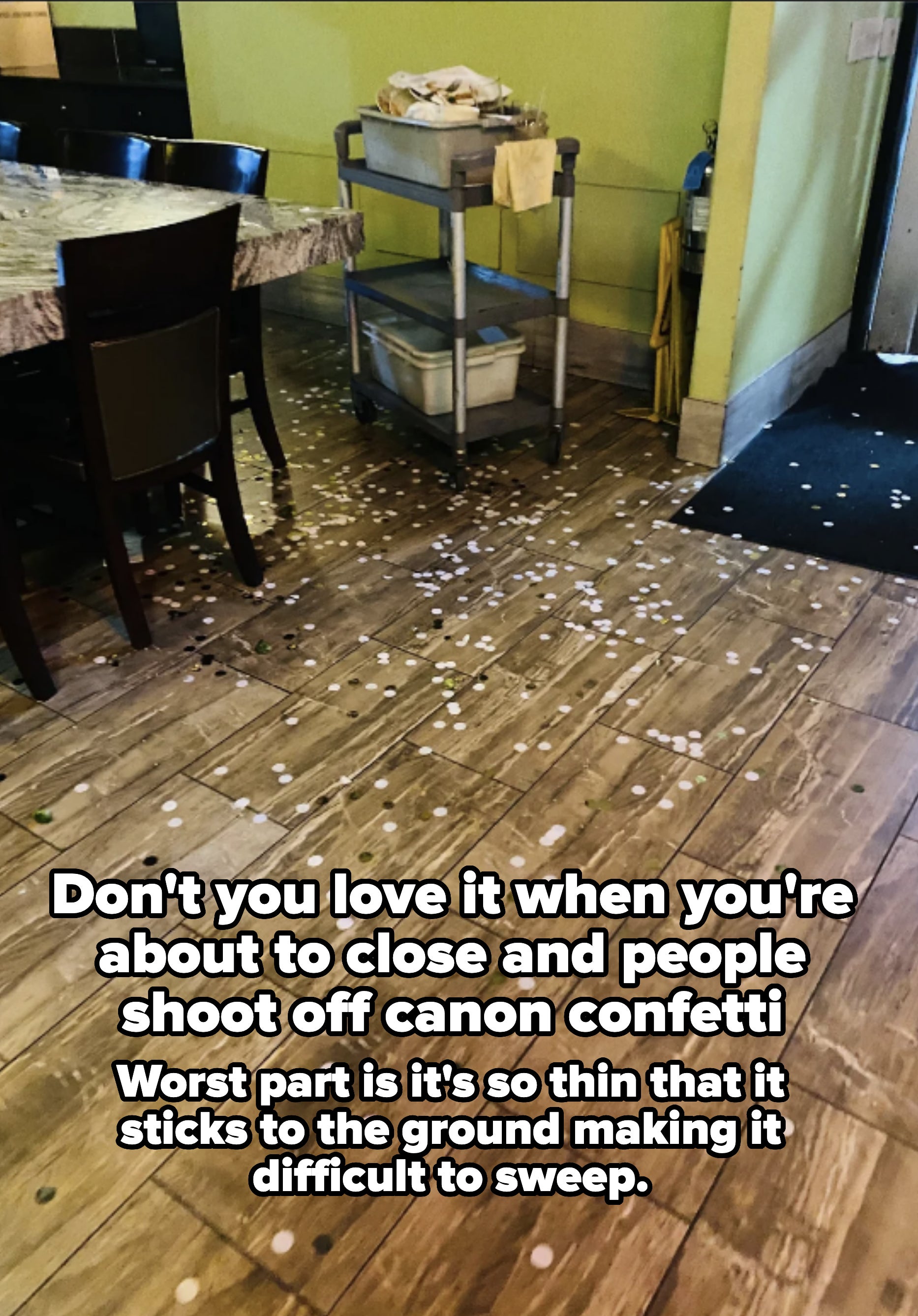 A restaurant floor scattered with confetti, in front of a table and a utility cart with cleaning supplies