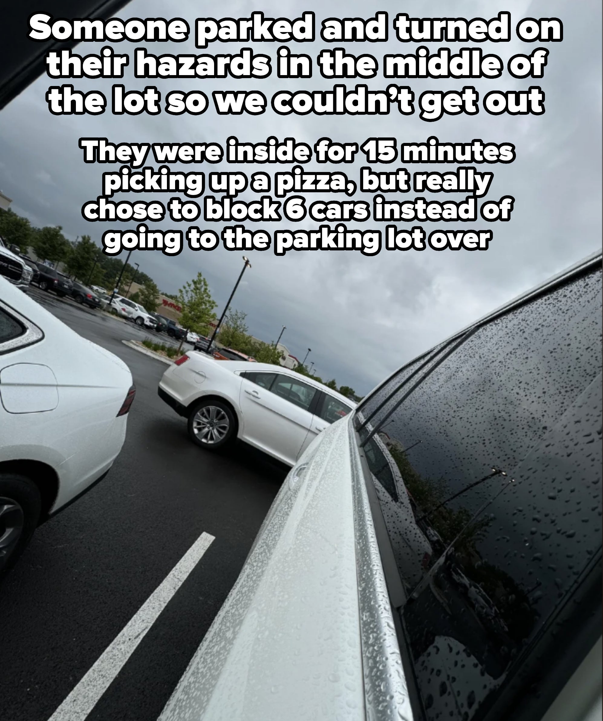 View from inside a car, showing raindrops on the window, with a few other cars parked outside and a cloudy sky above