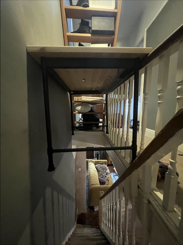 A person using an unconventional loft ladder set up indoors, climbing to an upper floor above a narrow staircase with white railings