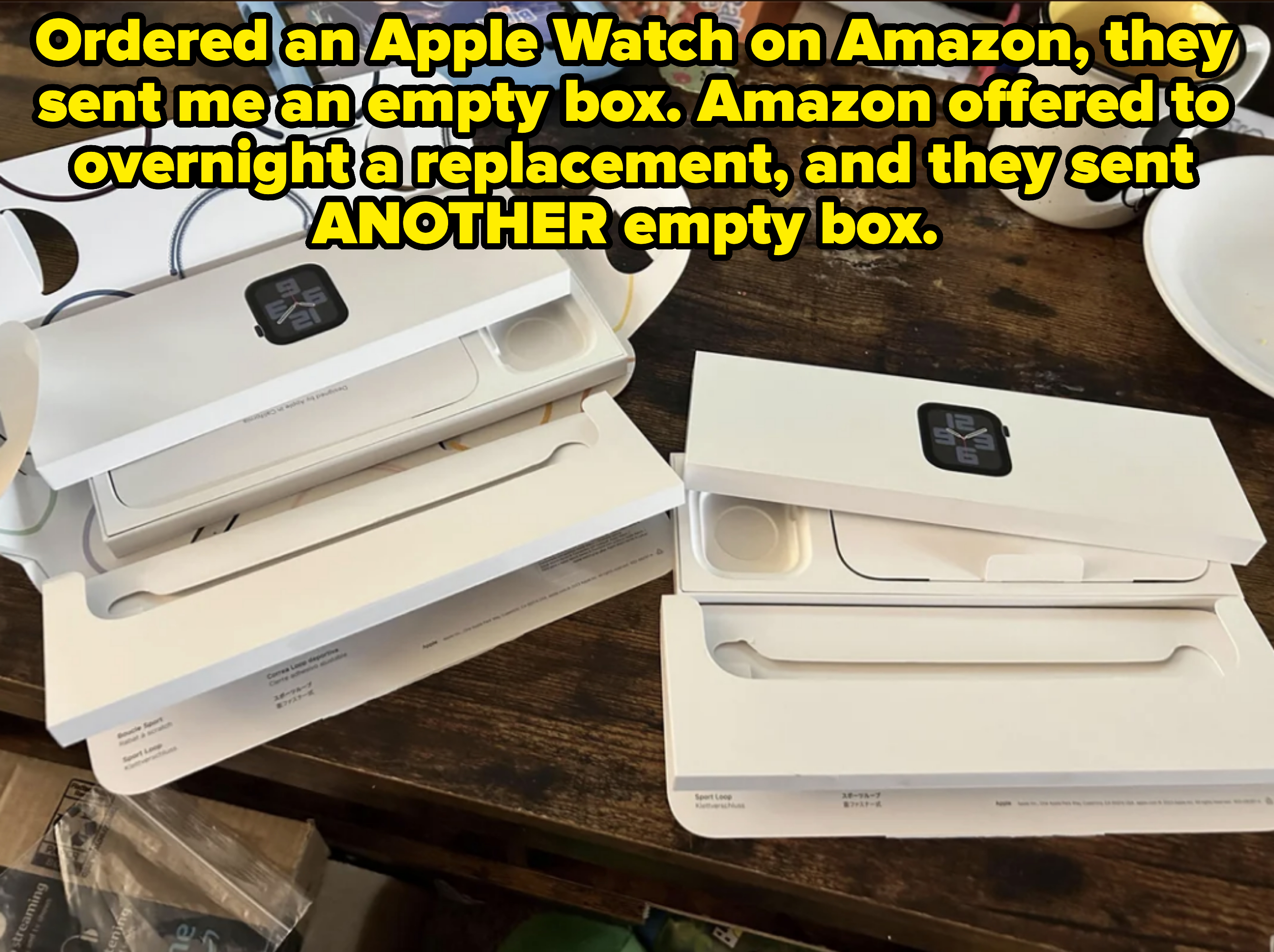 Two opened Apple Watch boxes, showing accessories inside, on a cluttered wooden table beside a mug and a plate