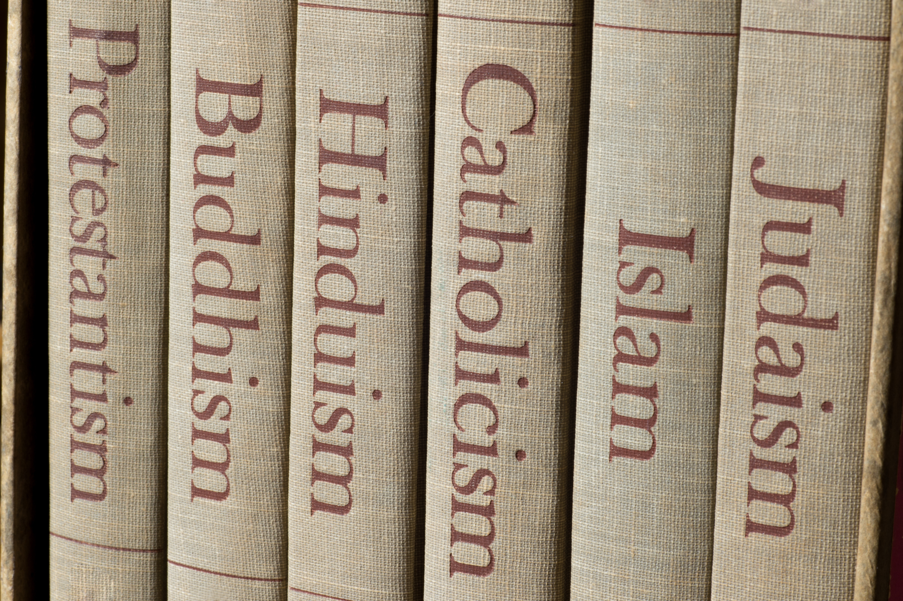 Books on a shelf, each with a title representing a major world religion: Protestantism, Buddhism, Hinduism, Catholicism, Islam, and Judaism