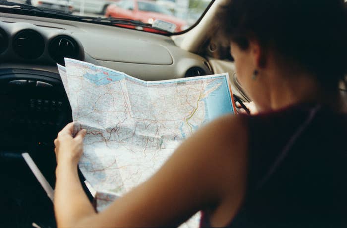 Person reading a road map while sitting in the passenger seat of a car. The image focuses on the unfolded map detailing various locations