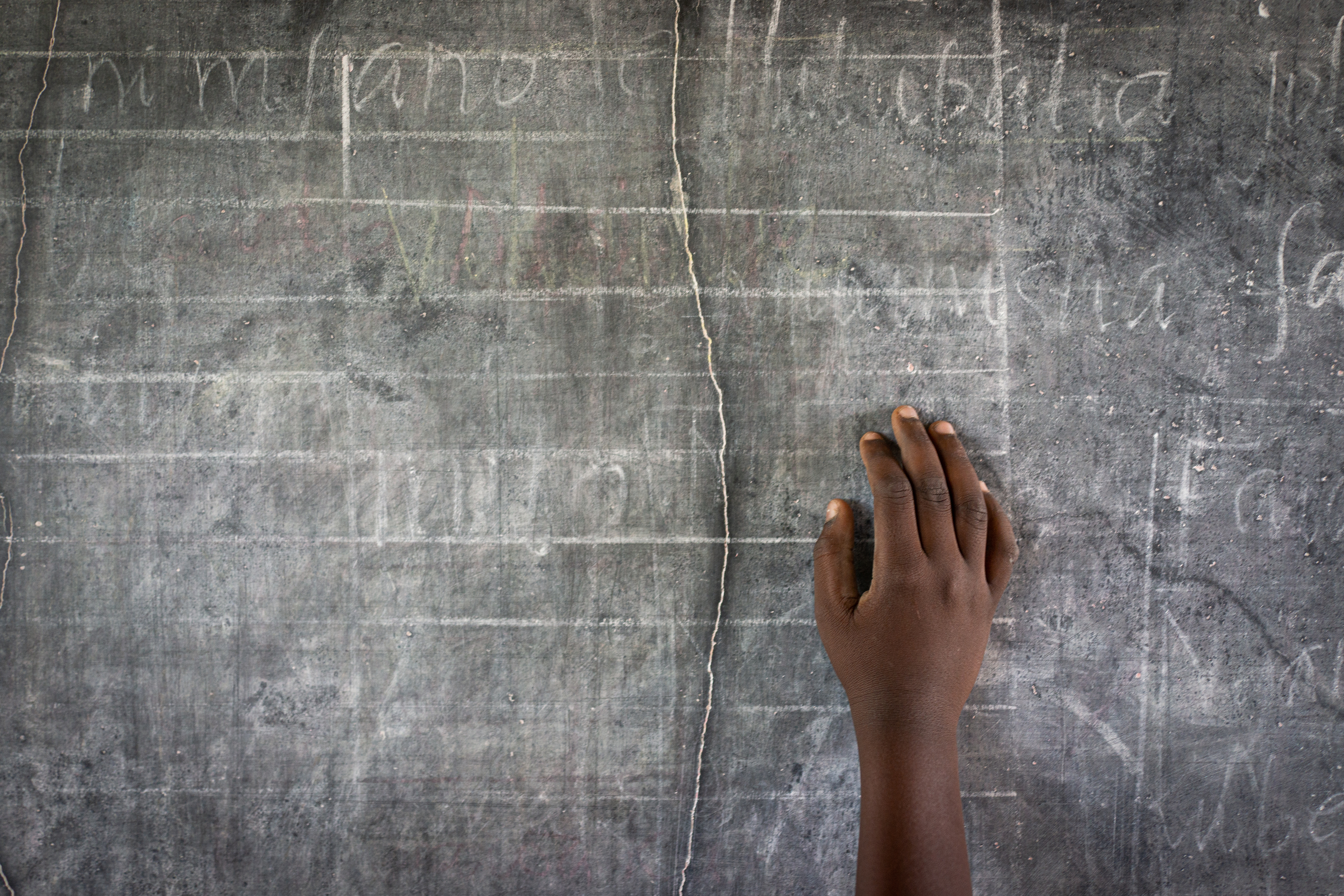 A child&#x27;s hand is seen writing on a chalkboard with faint text