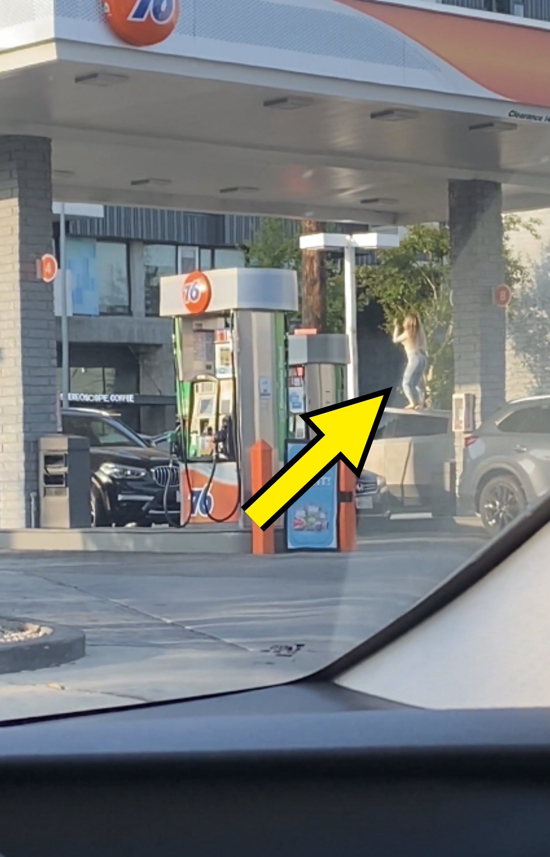 A person stands on top of an SUV at a gas station