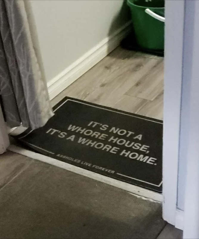 Doormat at the entrance of a home with the text: &quot;IT&#x27;S NOT A WHORE HOUSE, IT&#x27;S A WHORE HOME. ASSHOLES LIVE FOREVER.&quot;