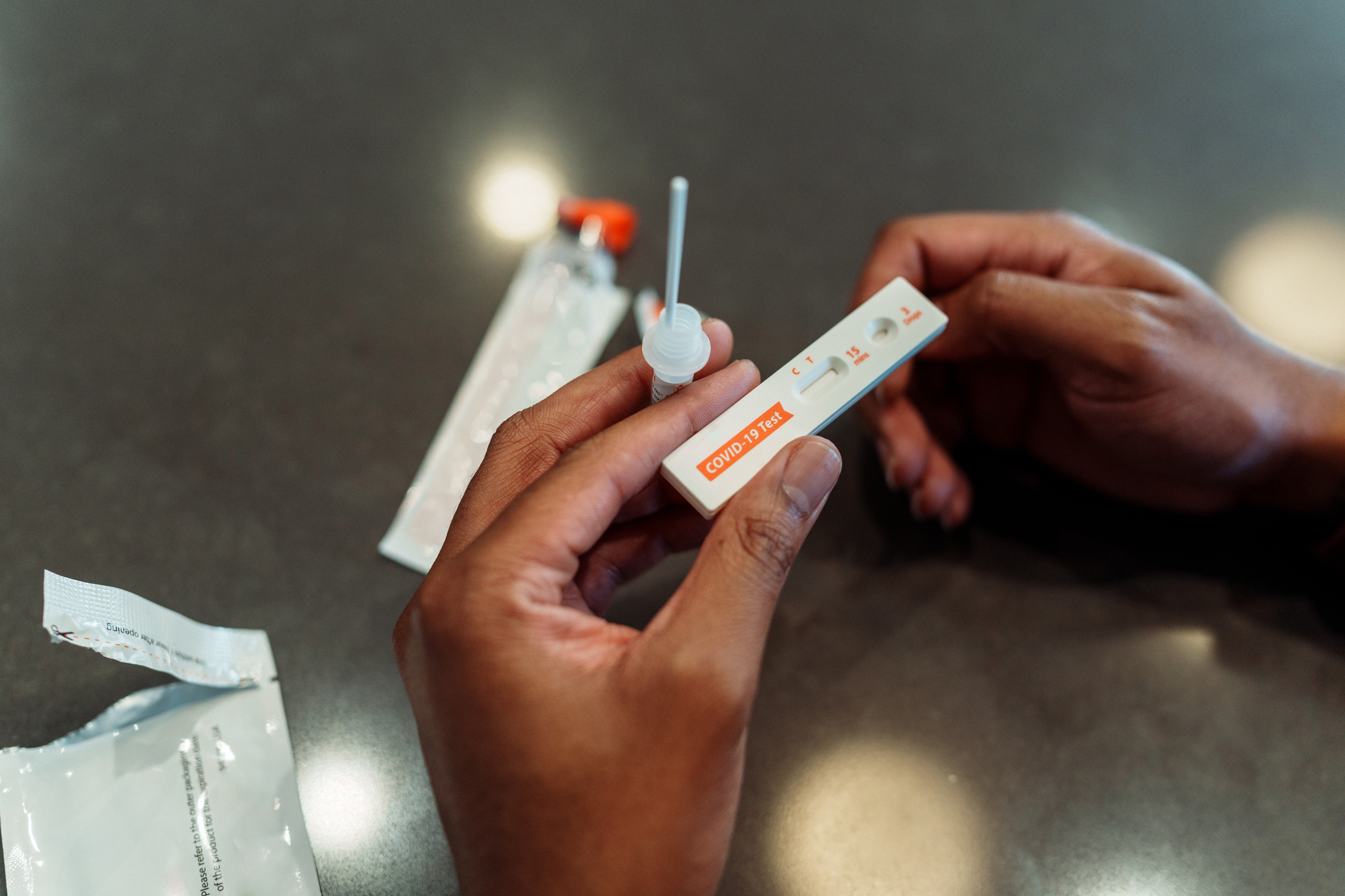 A person&#x27;s hands holding a COVID-19 home test kit, with test components including a swab and a vial on a table