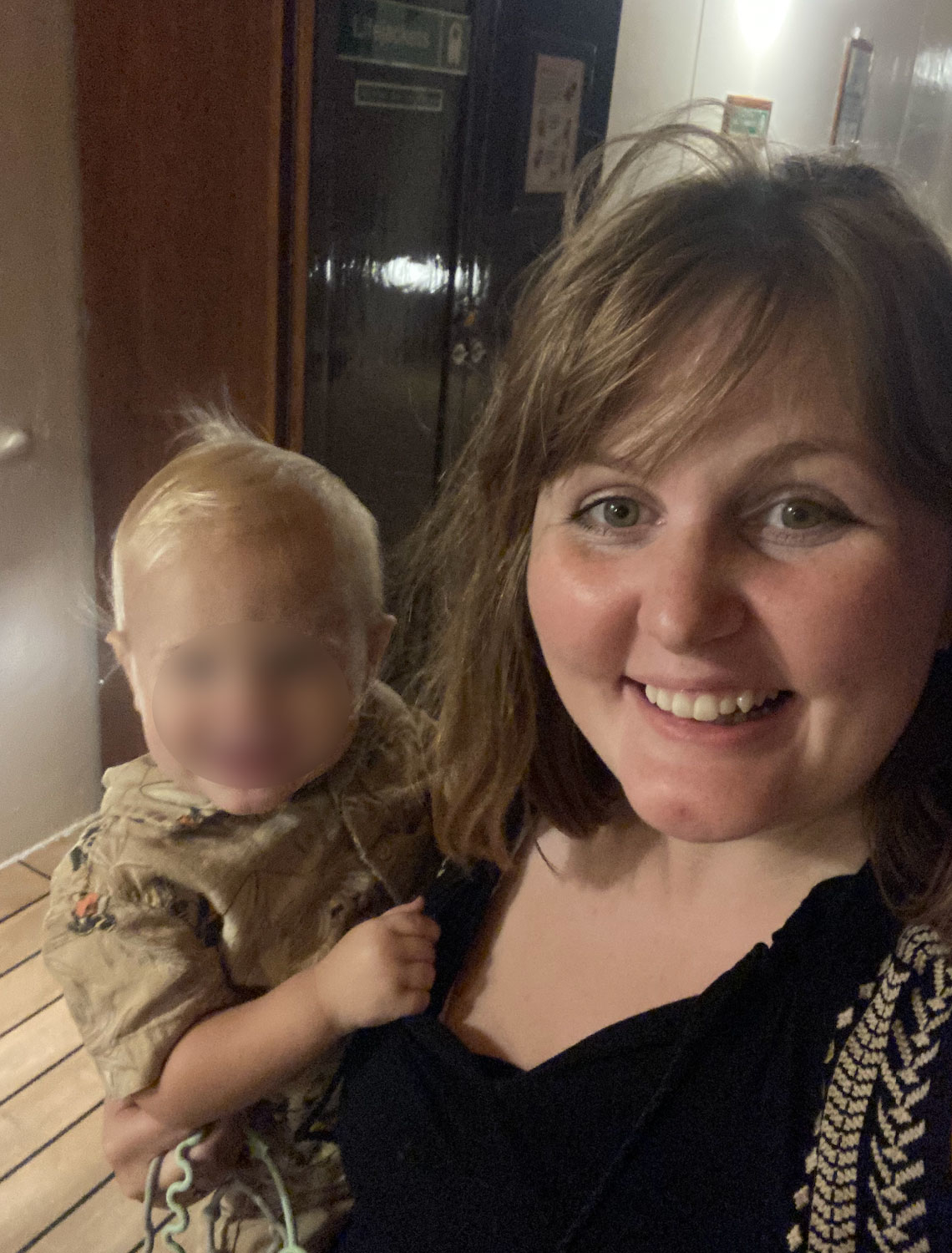 A woman smiling while holding a young child. The child&#x27;s face is blurred