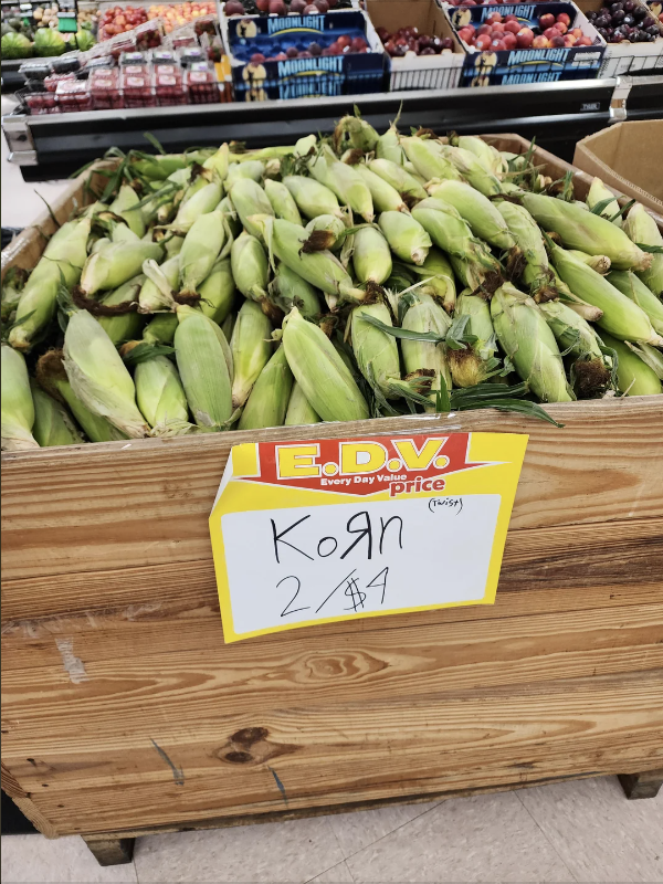 A grocery store display of fresh corn with a sign reading &quot;Korn, 2 for $4.&quot;