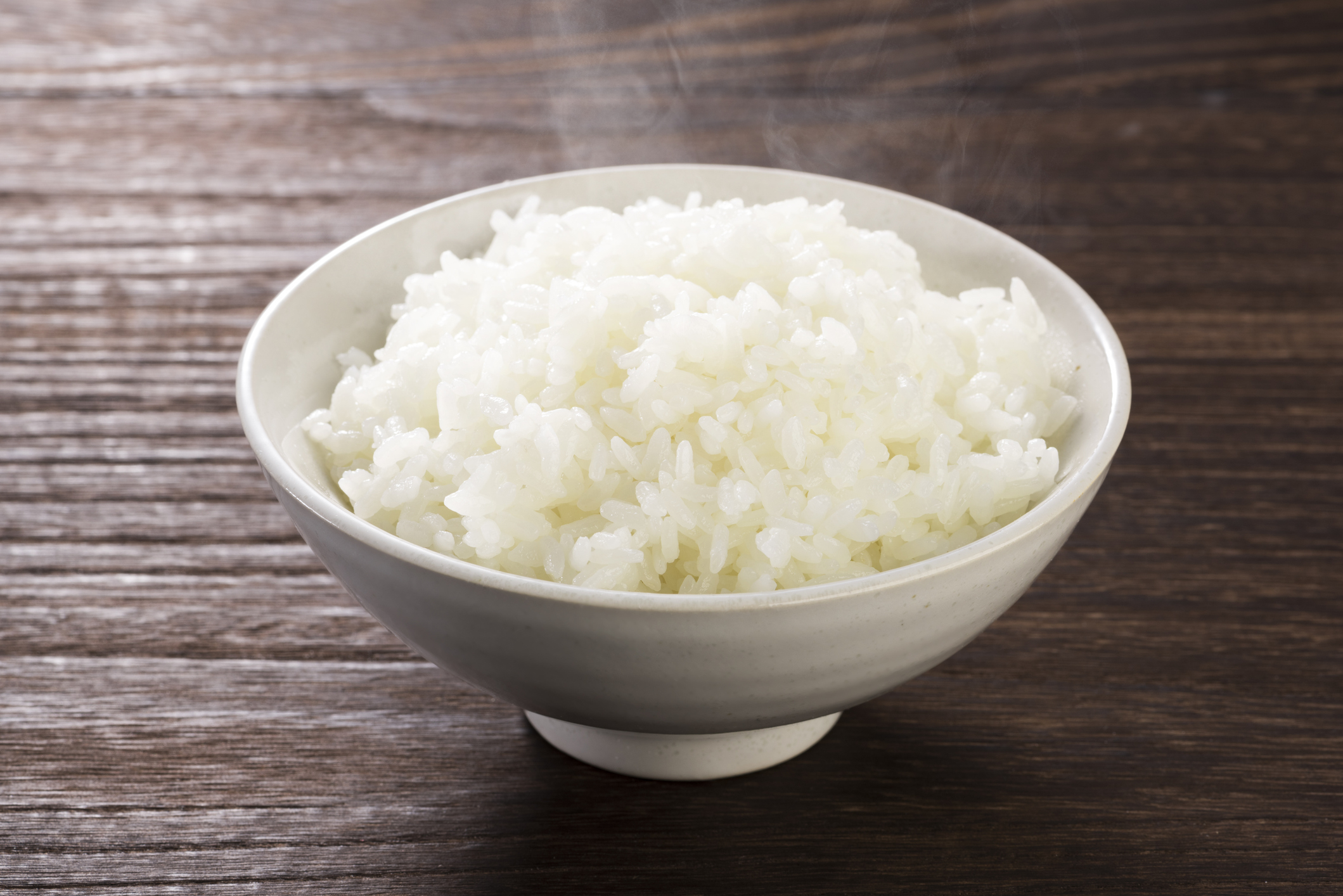 A steaming bowl of cooked rice on a wooden table