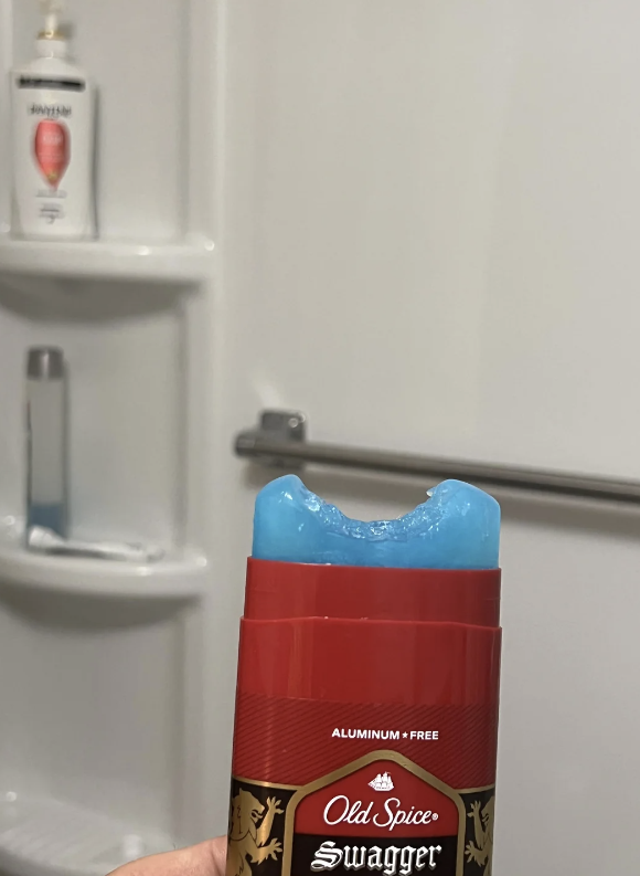 A stick of Old Spice Swagger deodorant with a bite mark. Shower products are visible on a bath shelf in the background