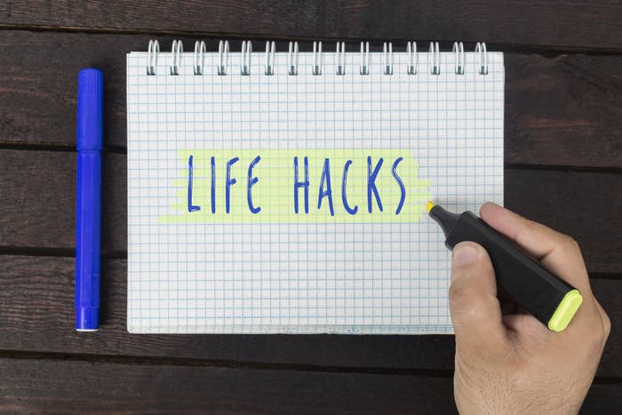 A hand highlights &quot;LIFE HACKS&quot; written on a spiral notepad with a blue marker, emphasizing self-improvement tips