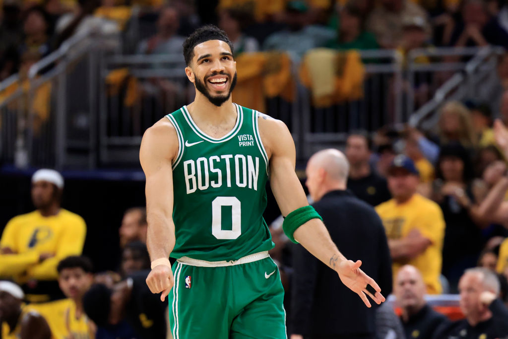 Jayson Tatum on the basketball court wearing a Boston Celtics jersey during a game, smiling and gesturing with both hands