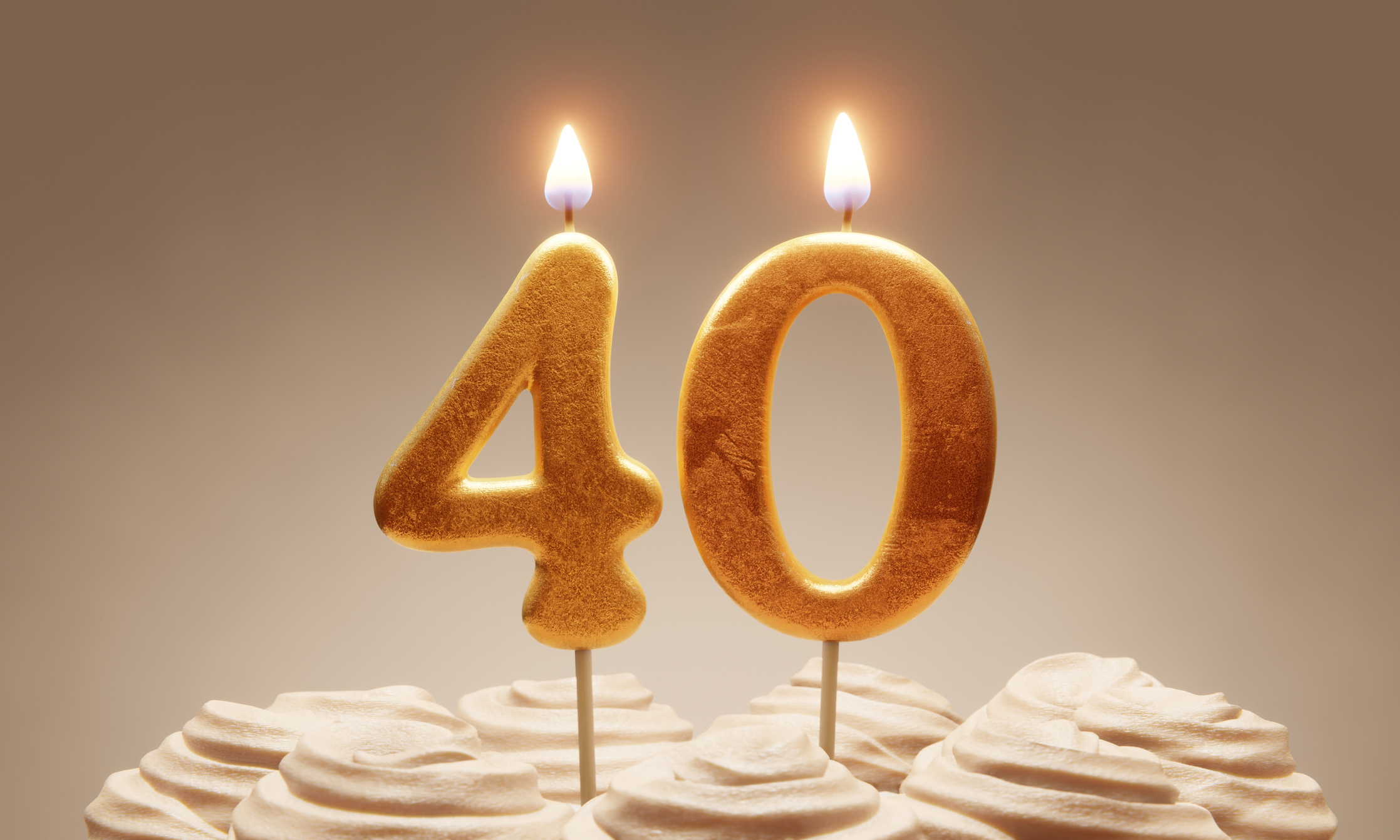 Lit golden candles shaped as number &#x27;40&#x27; on a cake topped with frosting swirls