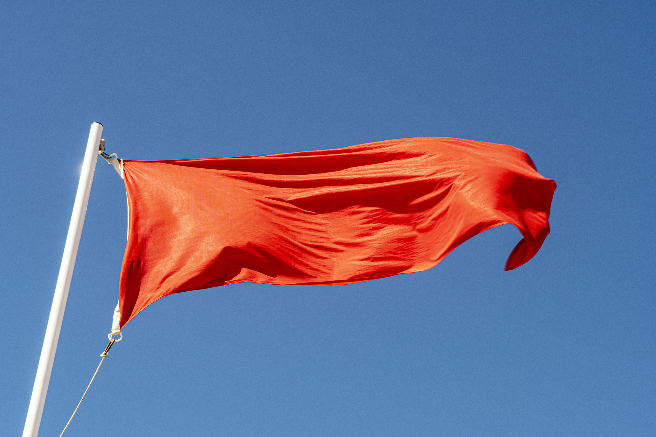 A red flag waves against a clear sky
