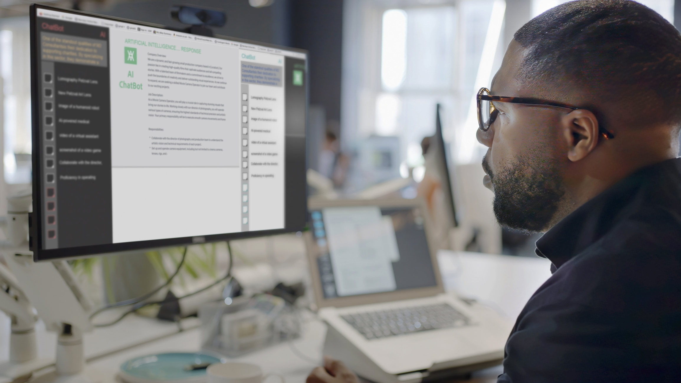 A person wearing glasses sits at a desk, working on a computer. A large monitor displays a document with text and checkboxes. The background shows an office setting