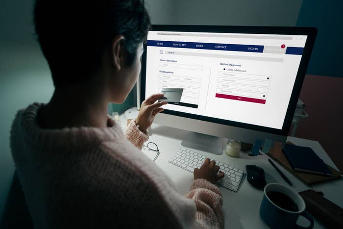 A person in a sweater is sitting at a desk, using a computer to enter payment information on a website