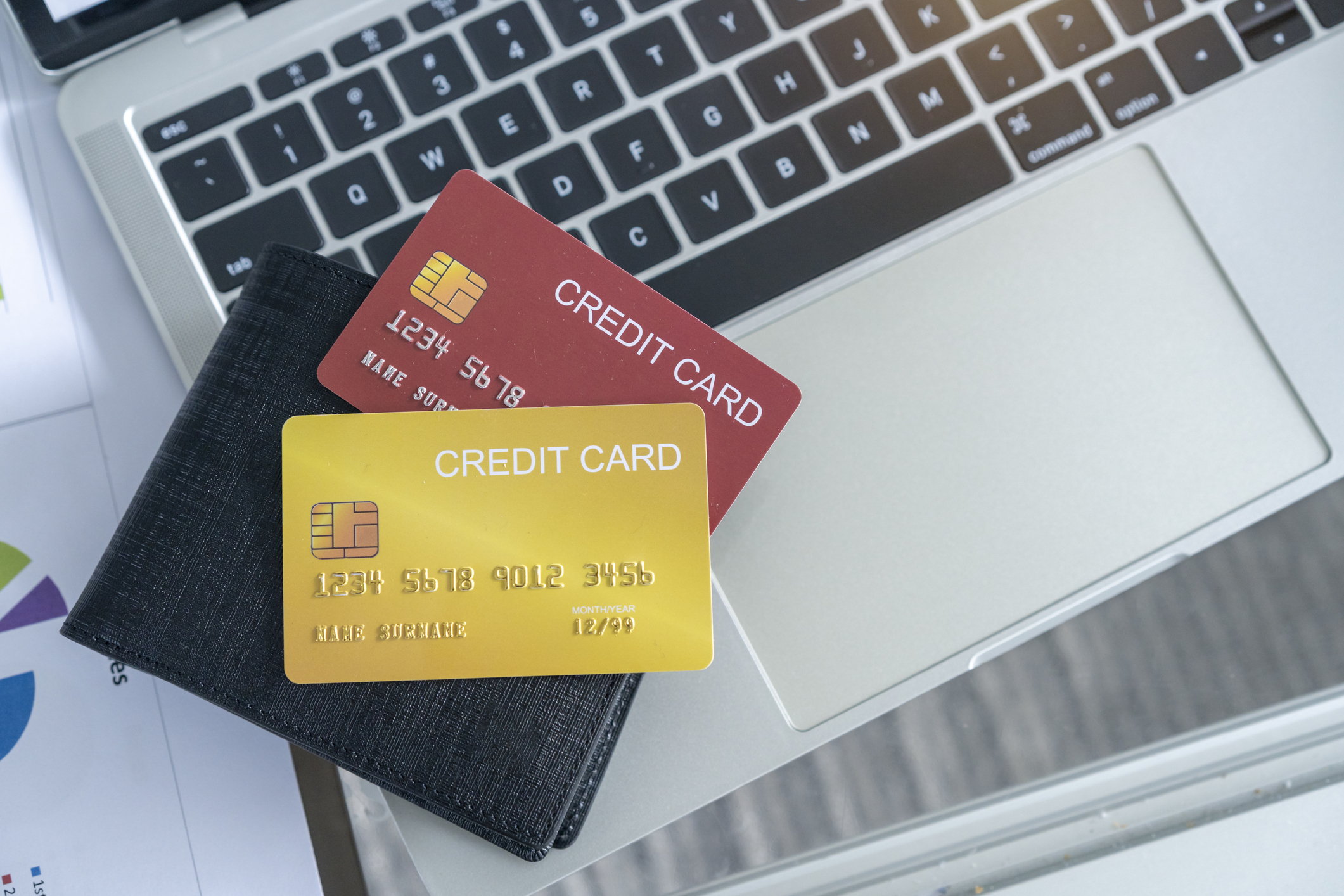 Two credit cards, one red and one yellow, partially inserted in a black wallet, placed on a laptop keyboard