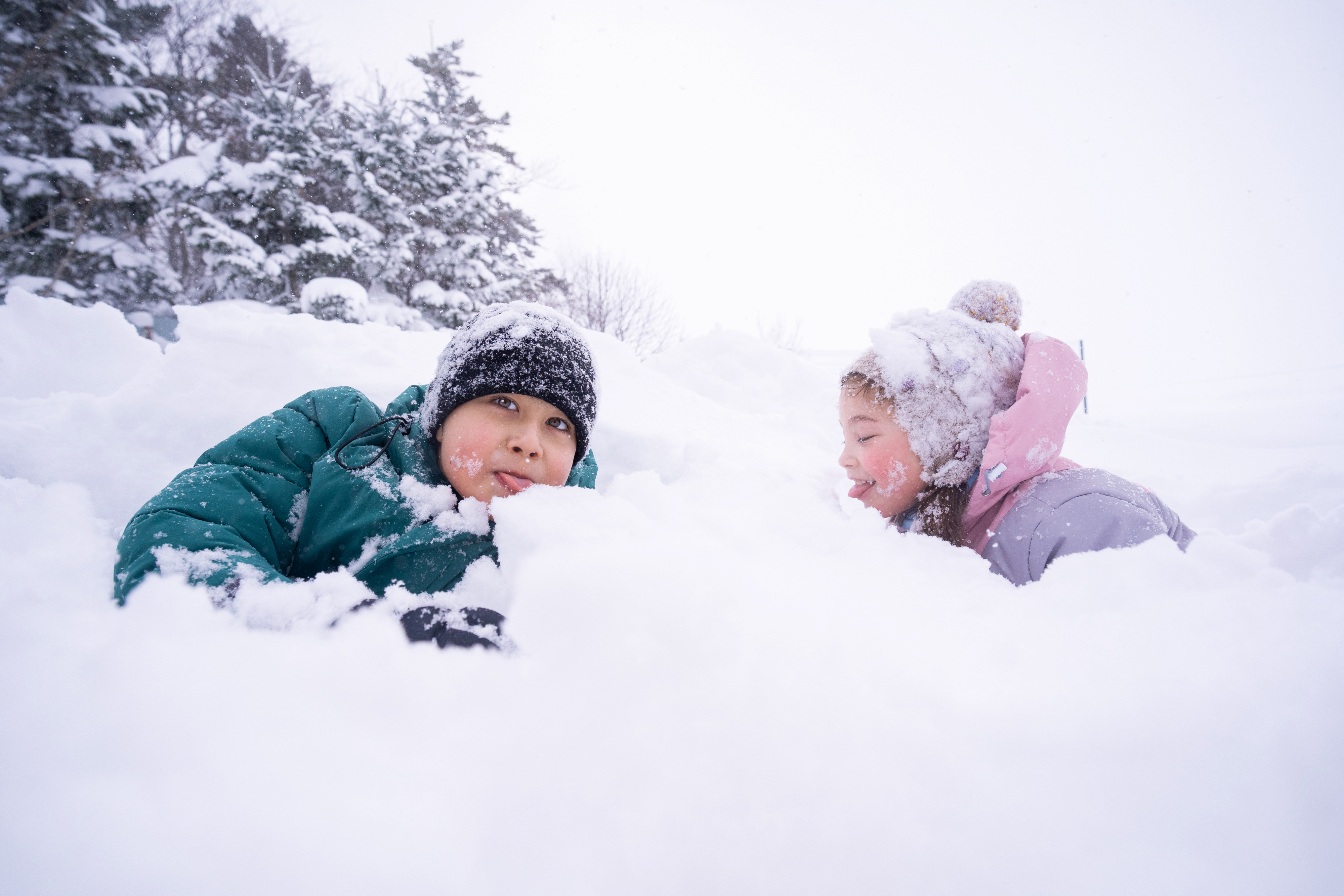 Two children bundled in winter coats and hats and playing in the snow