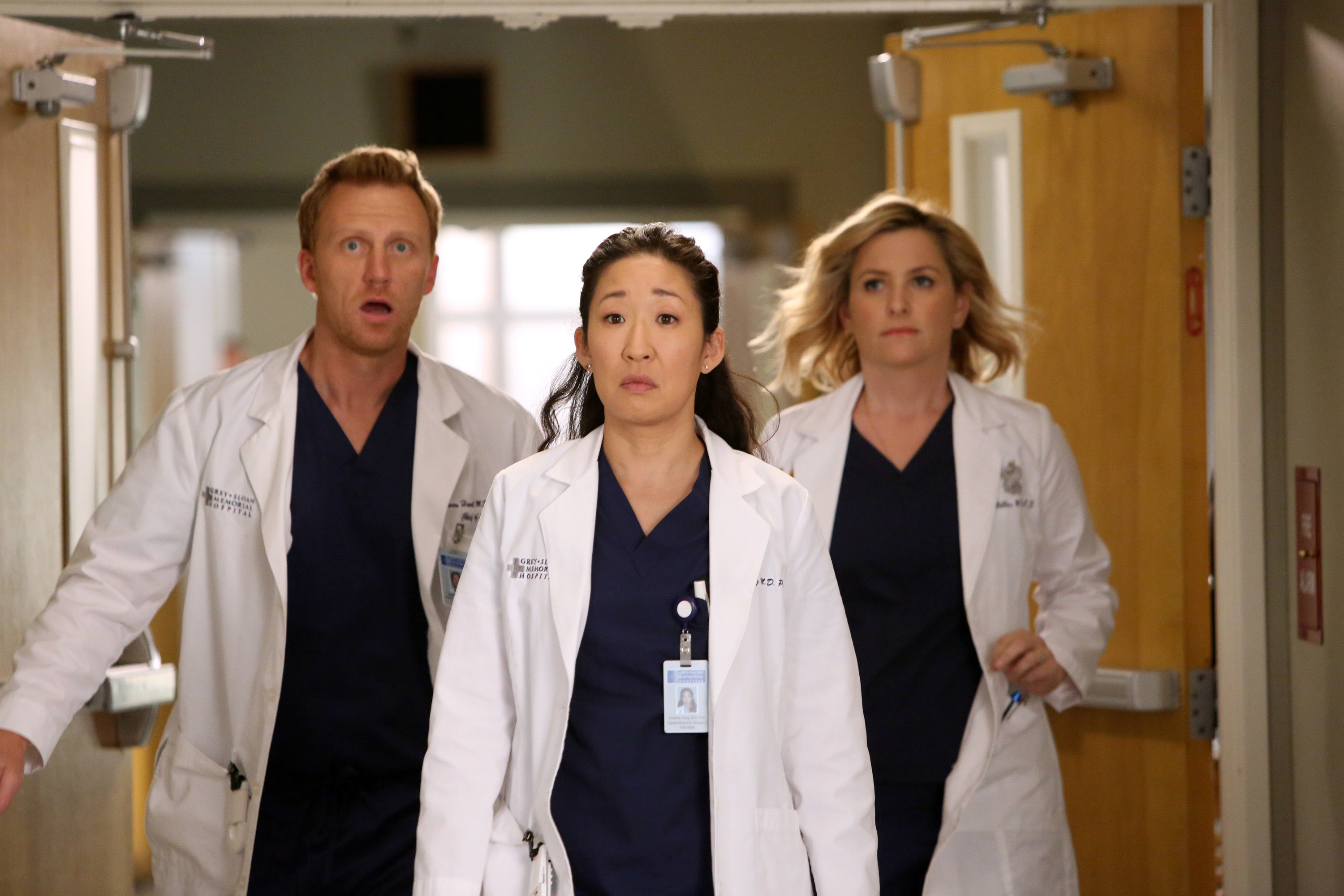 Kevin McKidd, Sandra Oh, and Jessica Capshaw in scrubs and white coats, appear to walk urgently through a hospital corridor