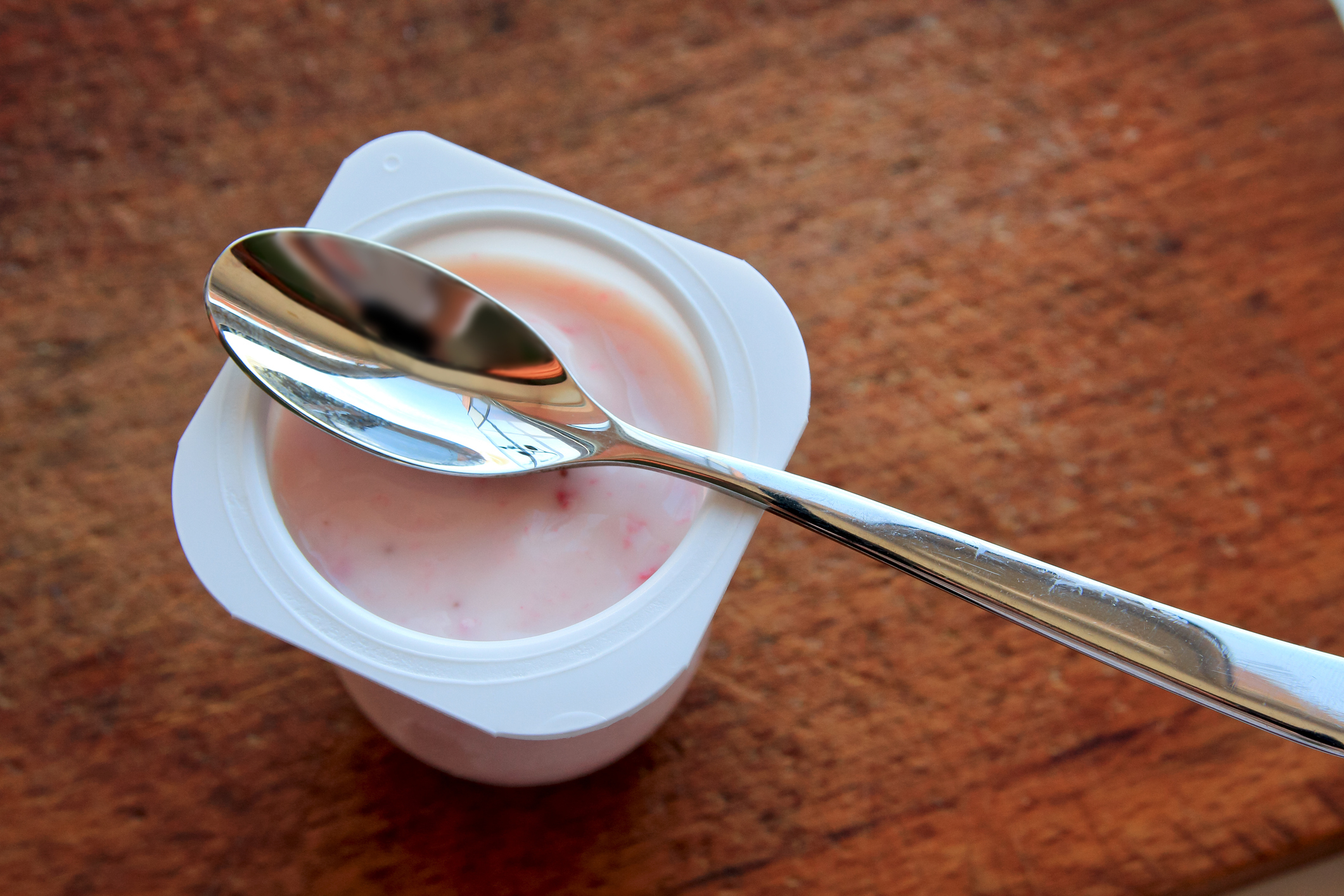 A yogurt container with a spoon resting on top, placed on a wooden surface