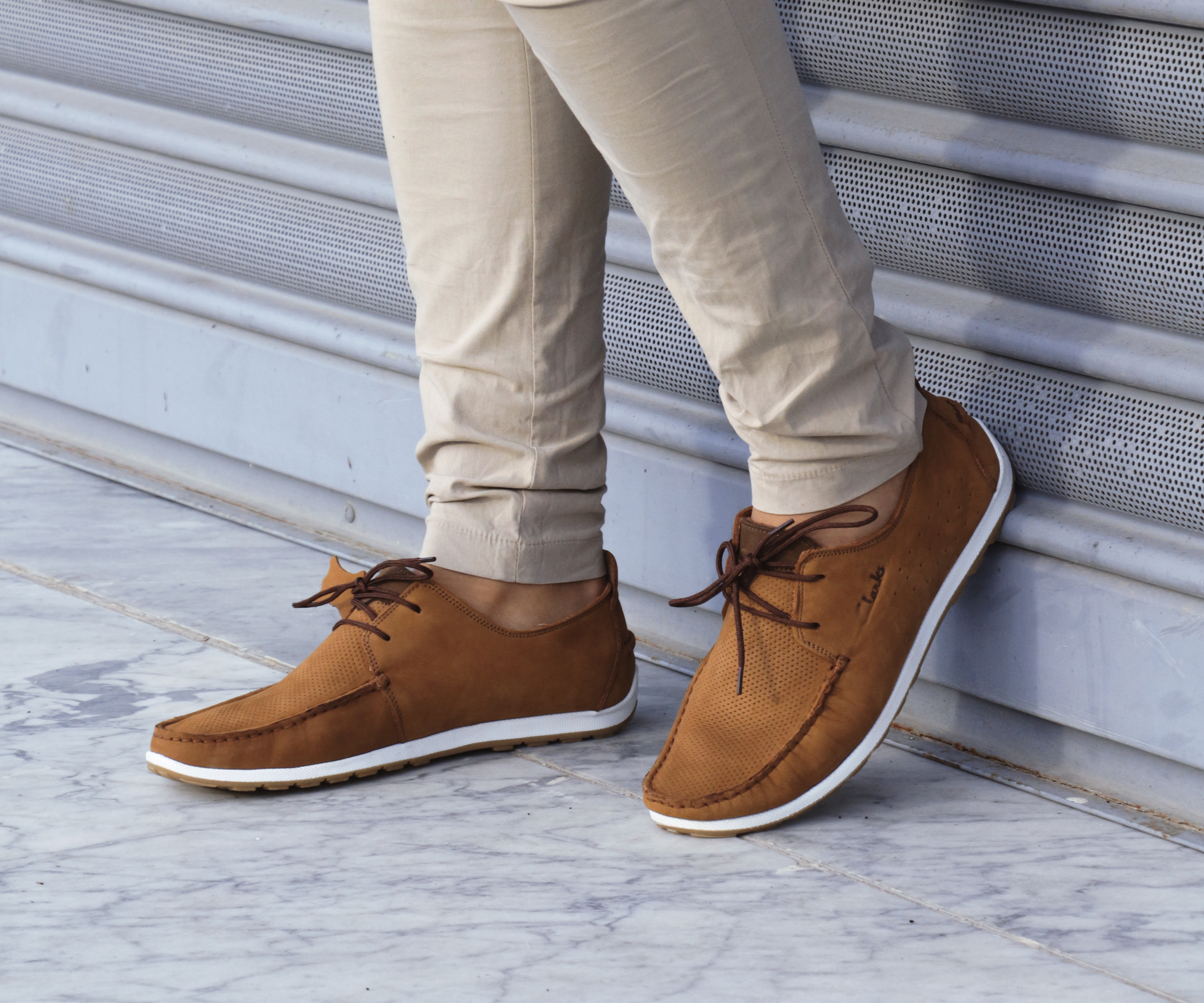 Person wearing tan pants and brown casual shoes with white soles standing near a metal shutter