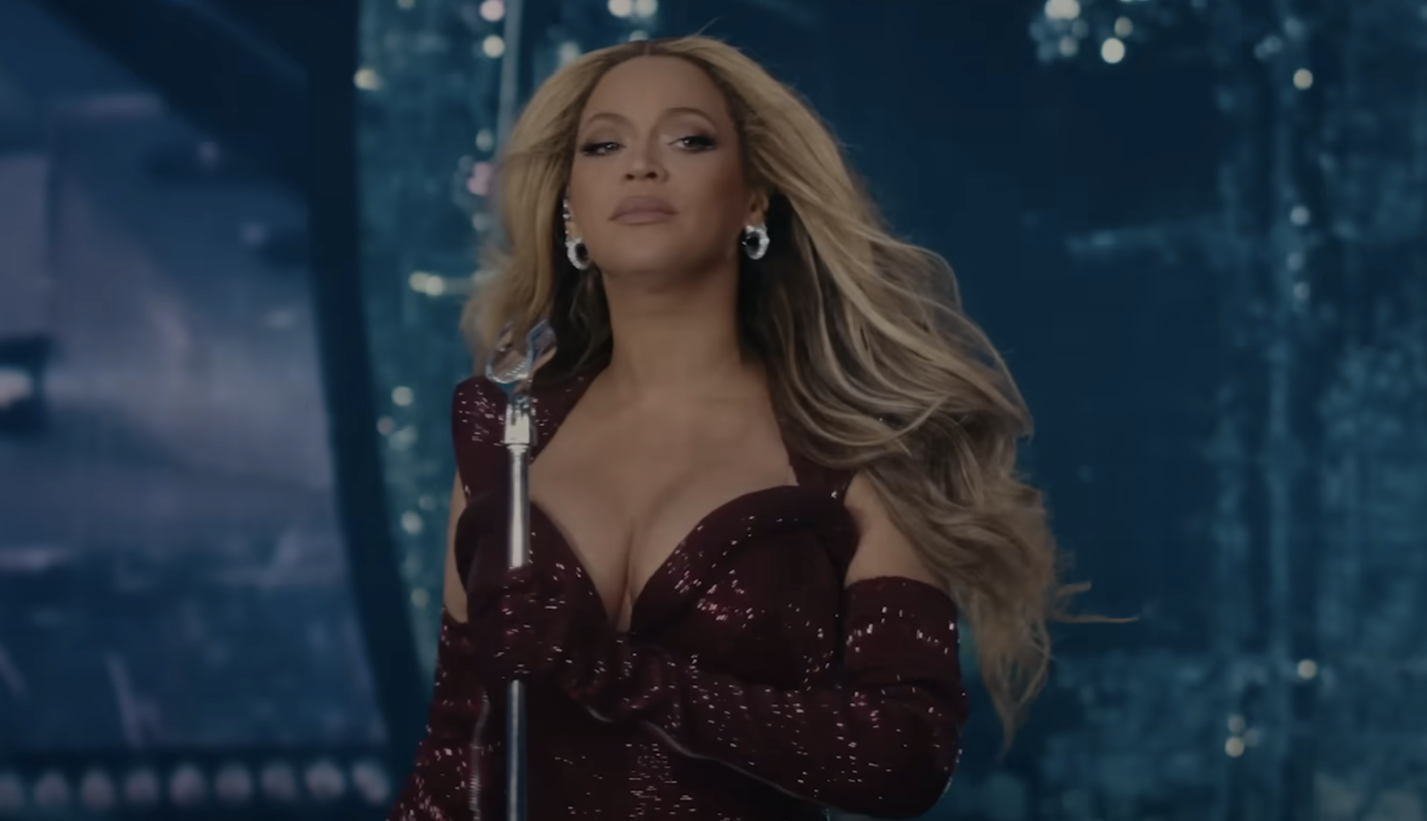 Beyoncé performs on stage, wearing a shimmering dress with matching gloves, holding a microphone