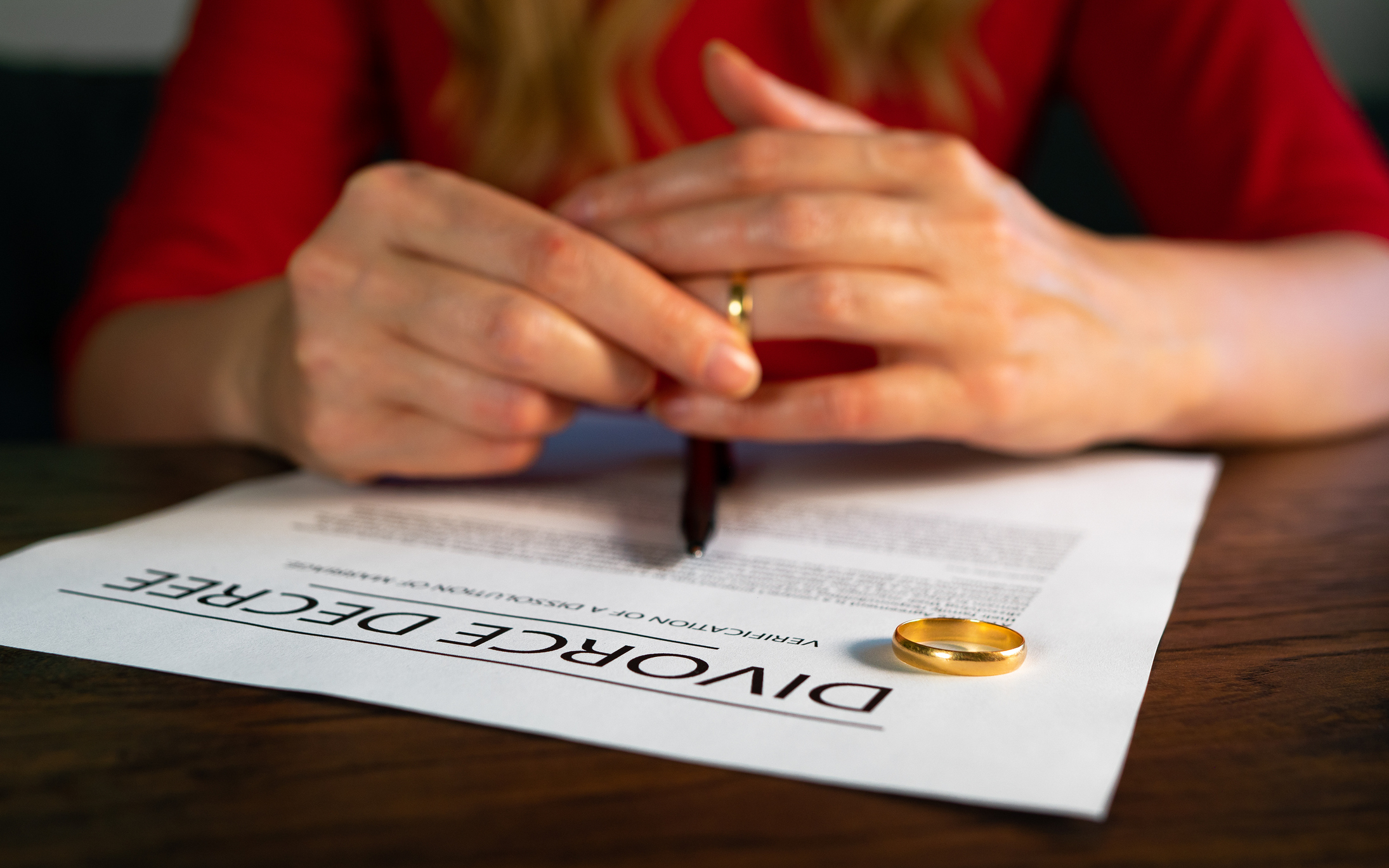 A close-up of hands with a wedding ring on the table, signing a divorce decree