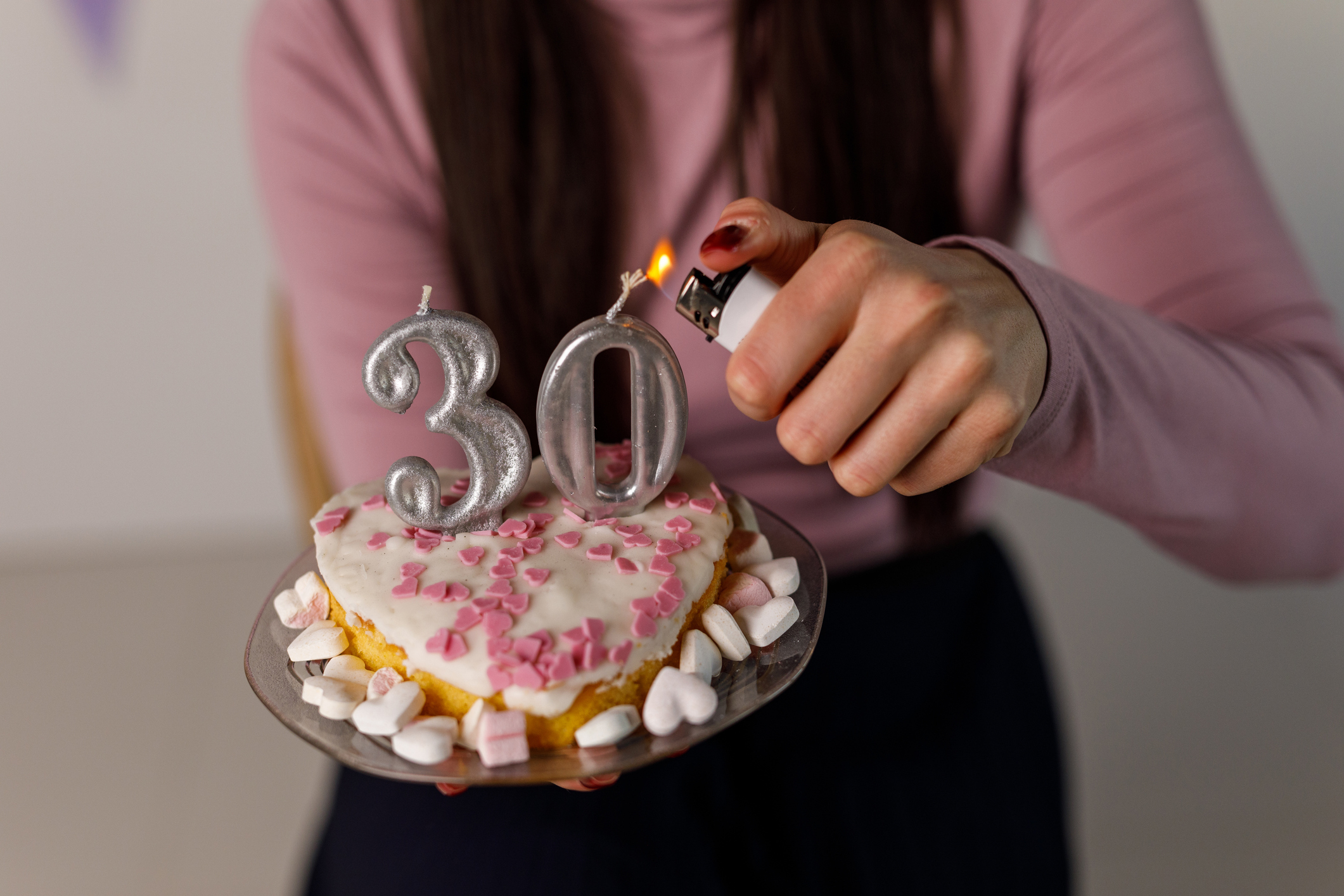 A person lights birthday candles shaped like the number 30 on a heart-shaped cake topped with small candies