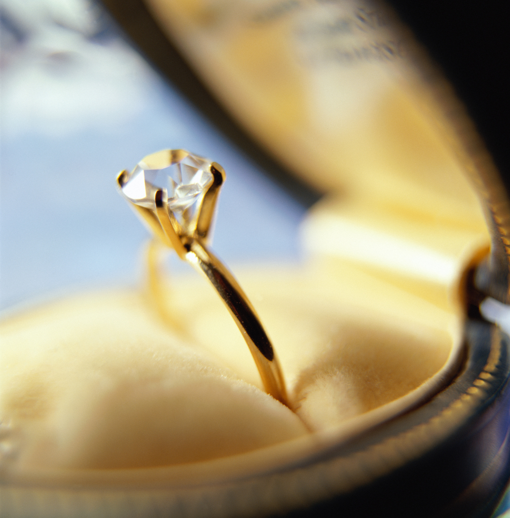 A close-up of a gold engagement ring with a single round-cut diamond displayed in an open ring box