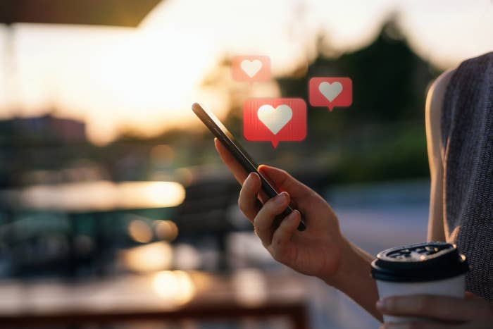 Person holding a smartphone with social media heart notifications above the screen while holding a takeaway coffee cup in the other hand