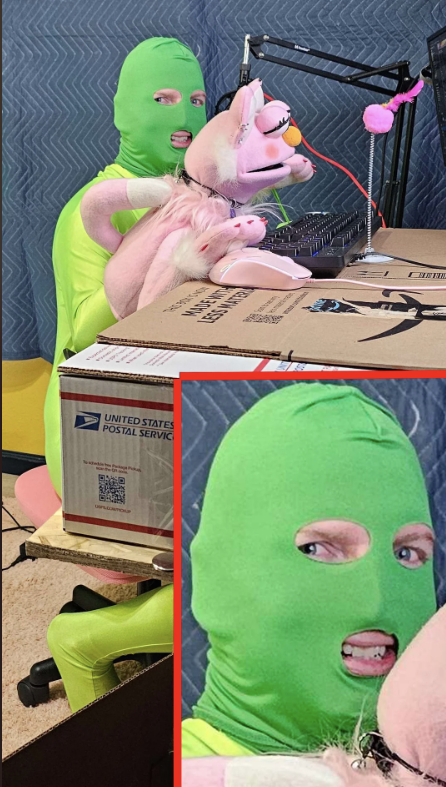 Person in a green spandex suit and balaclava holds a pink unicorn plush while speaking into a microphone at a desk with a cardboard box