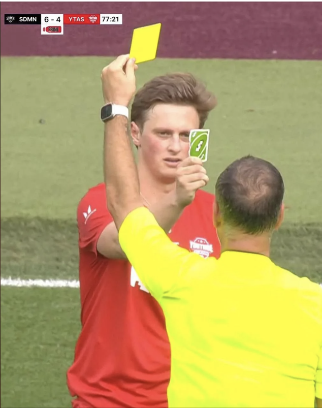 A soccer referee gives a yellow card while a player amusingly displays a green Uno reverse card. Scoreboard shows SDMN 6-4 YTAS with 77:21 on the clock