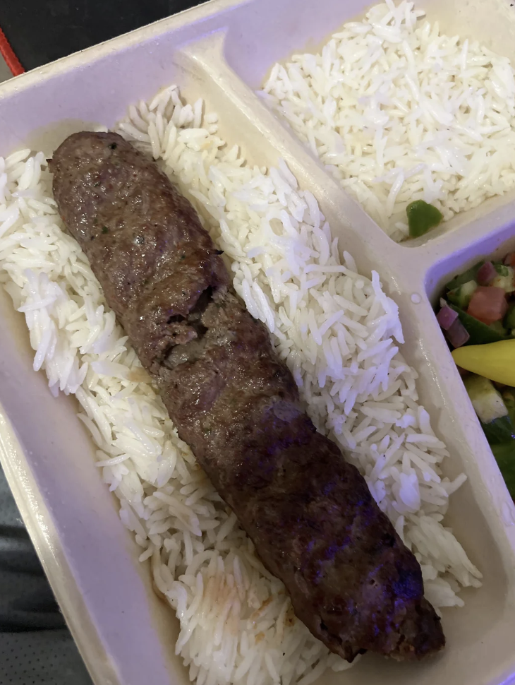 A divided food container with rice, a kebab over the rice, and a side of mixed vegetables