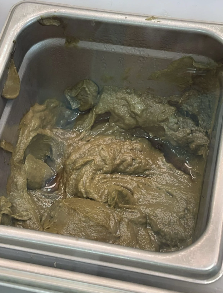 A metal container filled with a thick, mushy, unidentifiable greenish-brown substance