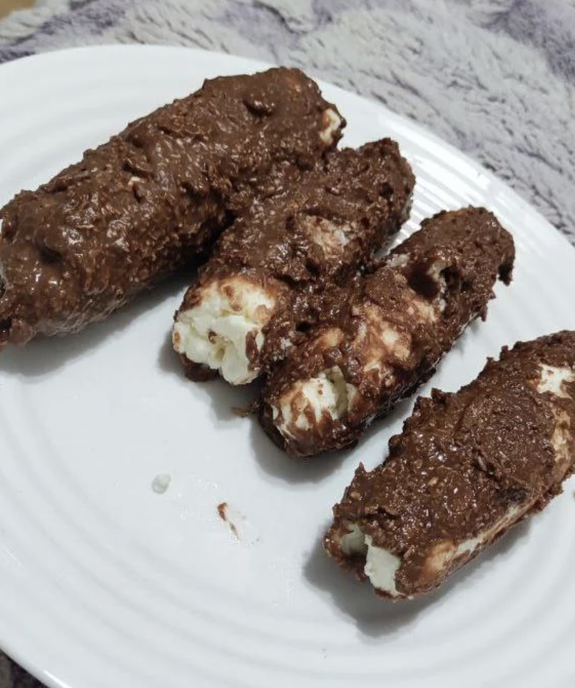 Four chocolate-coated snack bars with exposed white centers on a white plate