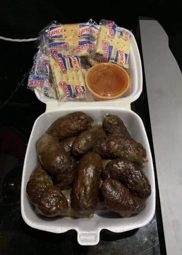 A takeout container filled with fried food, a cup of sauce, and packages of Lance Saltine crackers