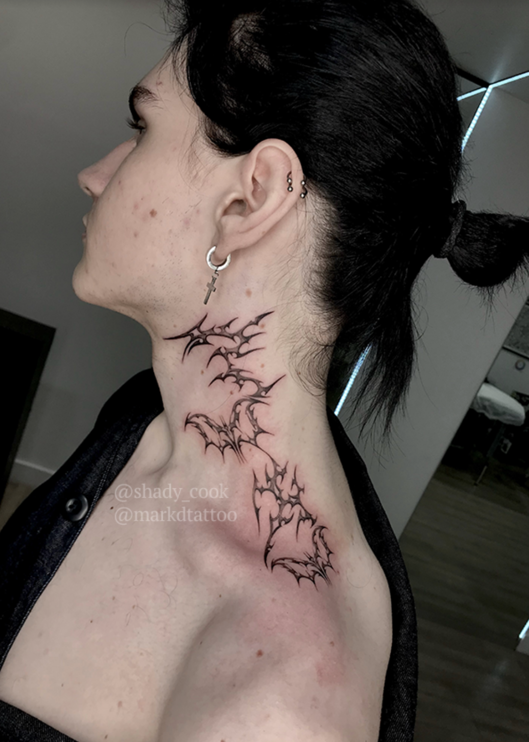 Side view of a person&#x27;s neck with intricate tattoo art featuring jagged bat shapes from below the ear to the shoulder. The person&#x27;s hair is tied back. Tattoos by @shady_cook and @markdtattoo